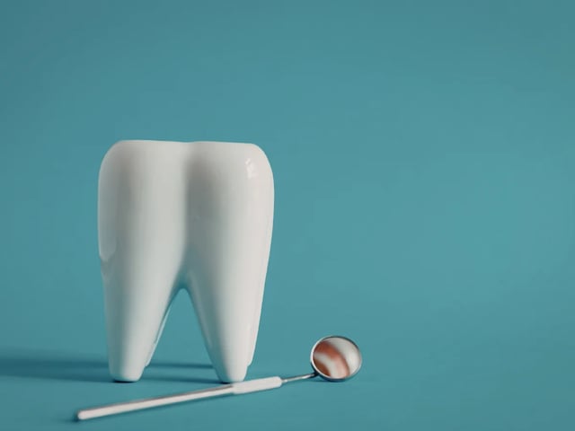 White ceramic tooth model and dental mirror on a teal background representing emergency broken tooth repair