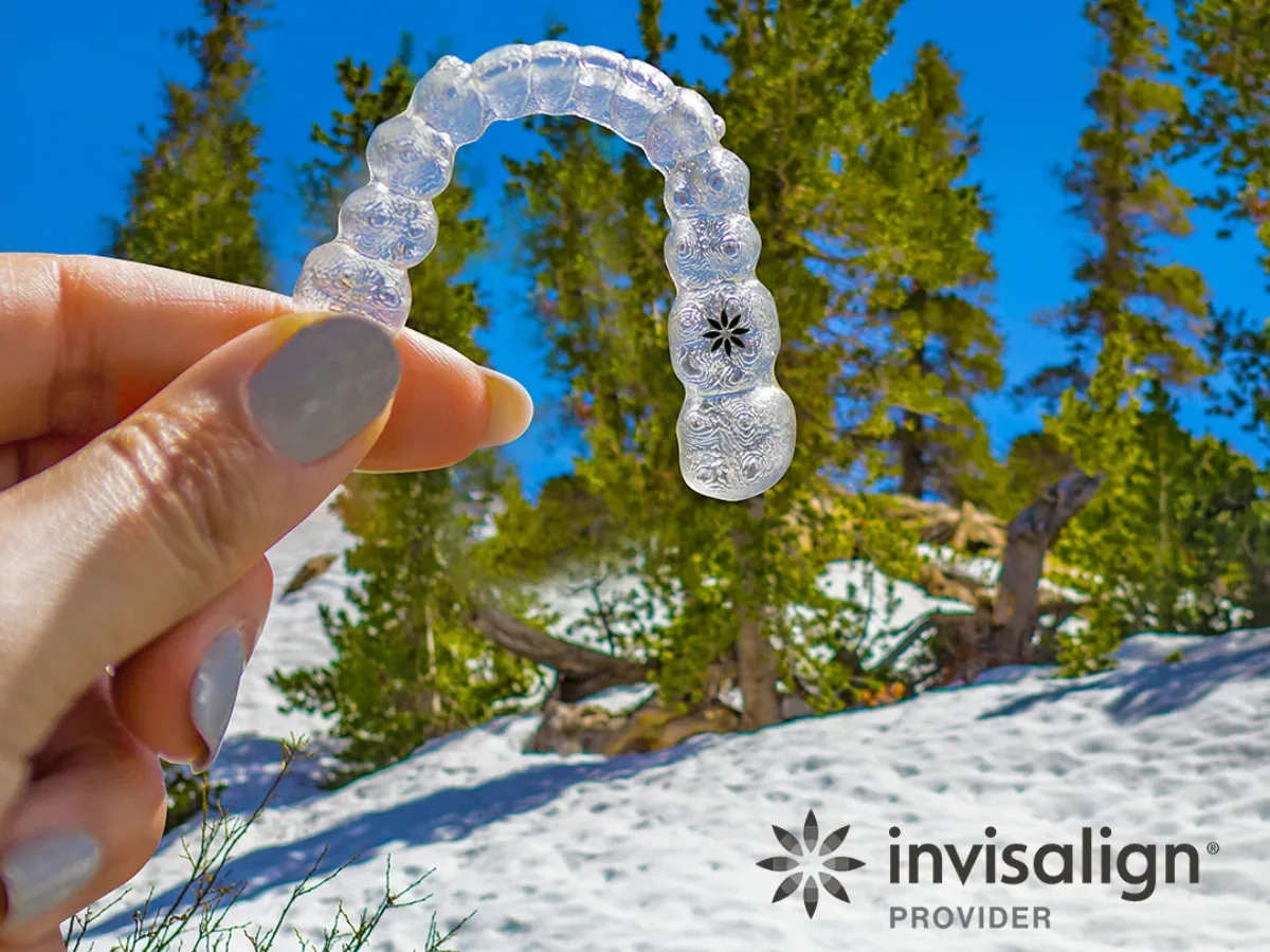 Invisalign Dentist: Advanced Complex Case Techniques | North Toronto Dental Centre Hand holding a clear Invisalign aligner outdoors with snowy mountain backdrop and Invisalign Provider logo