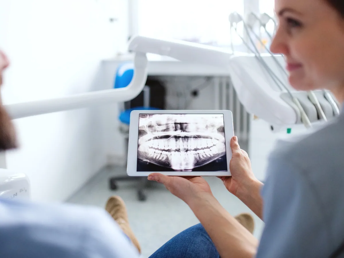 Dentist on Avenue Rd: What Your X-Rays Reveal | North Toronto Dental Centre Dentist reviewing a digital panoramic X-ray with a patient on a tablet in a modern dental office