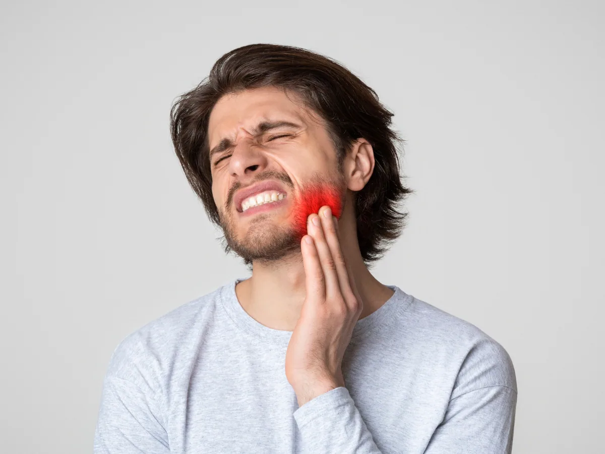 Emergency Dentist on Avenue Road: Abscess Treatment | North Toronto Dental Centre Young man holding his jaw in pain with red highlight indicating dental abscess swelling